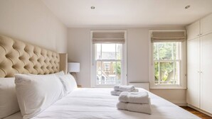 A large bed with a tufted headboard, white linens, and two rolled towels on the bed.