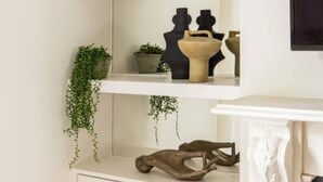 A white wall with a white shelf unit holding decorative items and a hanging plant.