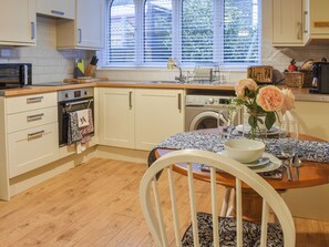 A kitchen with a dining area, wooden cabinets, a washing machine, and a window with blinds.