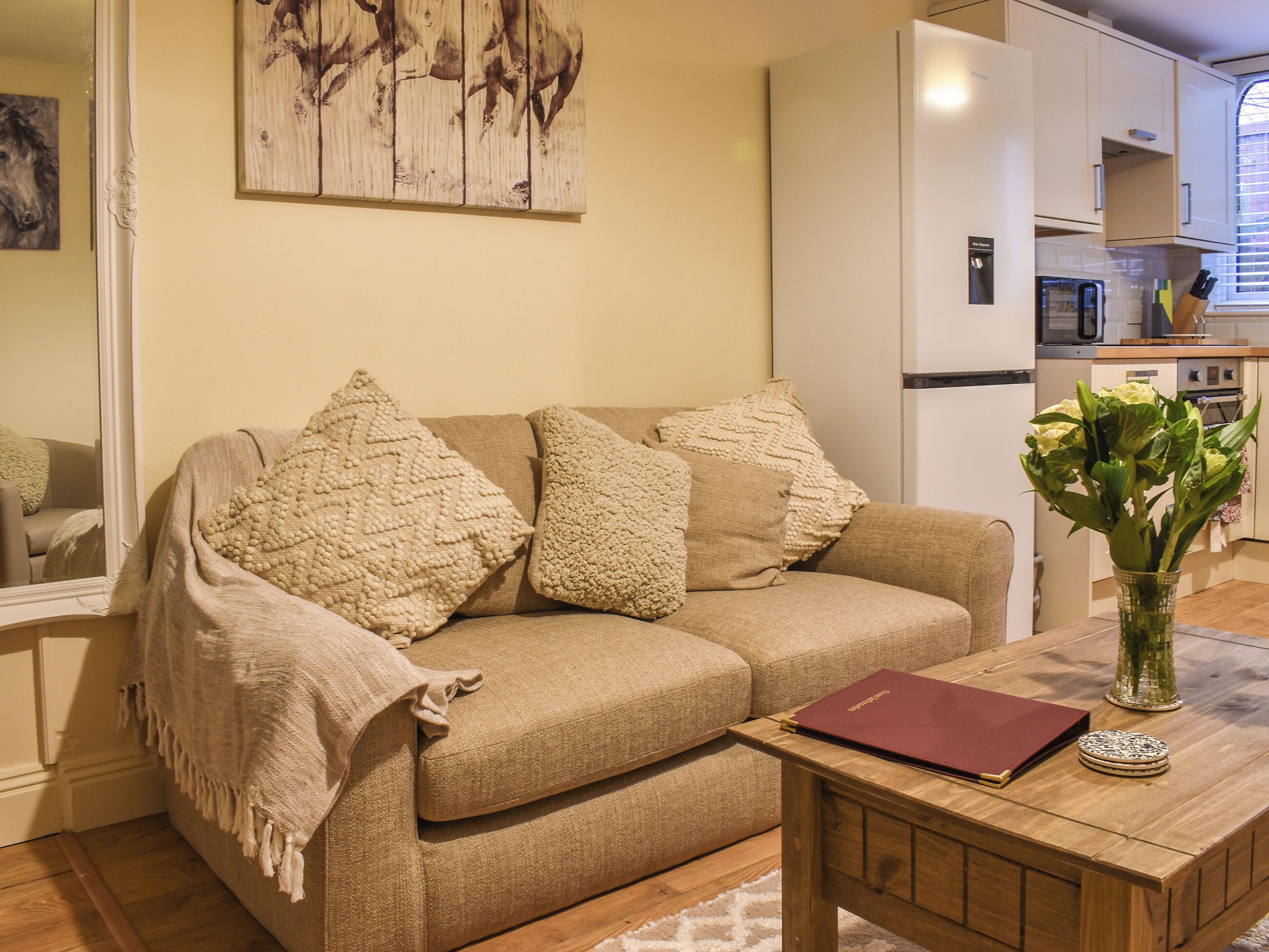 A living room with a sofa, a coffee table, a mirror, and a kitchen in the background.