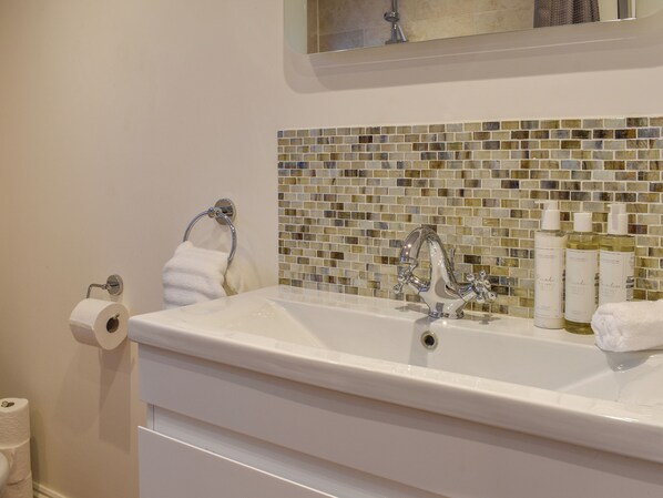 A bathroom with a white sink, a glass mosaic backsplash, a silver faucet, and three bottles of hand soap. - South Wing Coldharbour Park Farm (Liss)