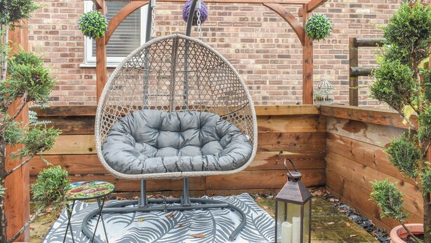 Een houten pergola met een hangstoel, een lantaarn en potplanten.
