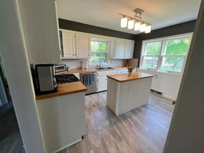 Une cuisine moderne avec des meubles blancs, un îlot central, un four encastré et une fenêtre donnant sur un espace verdoyant.