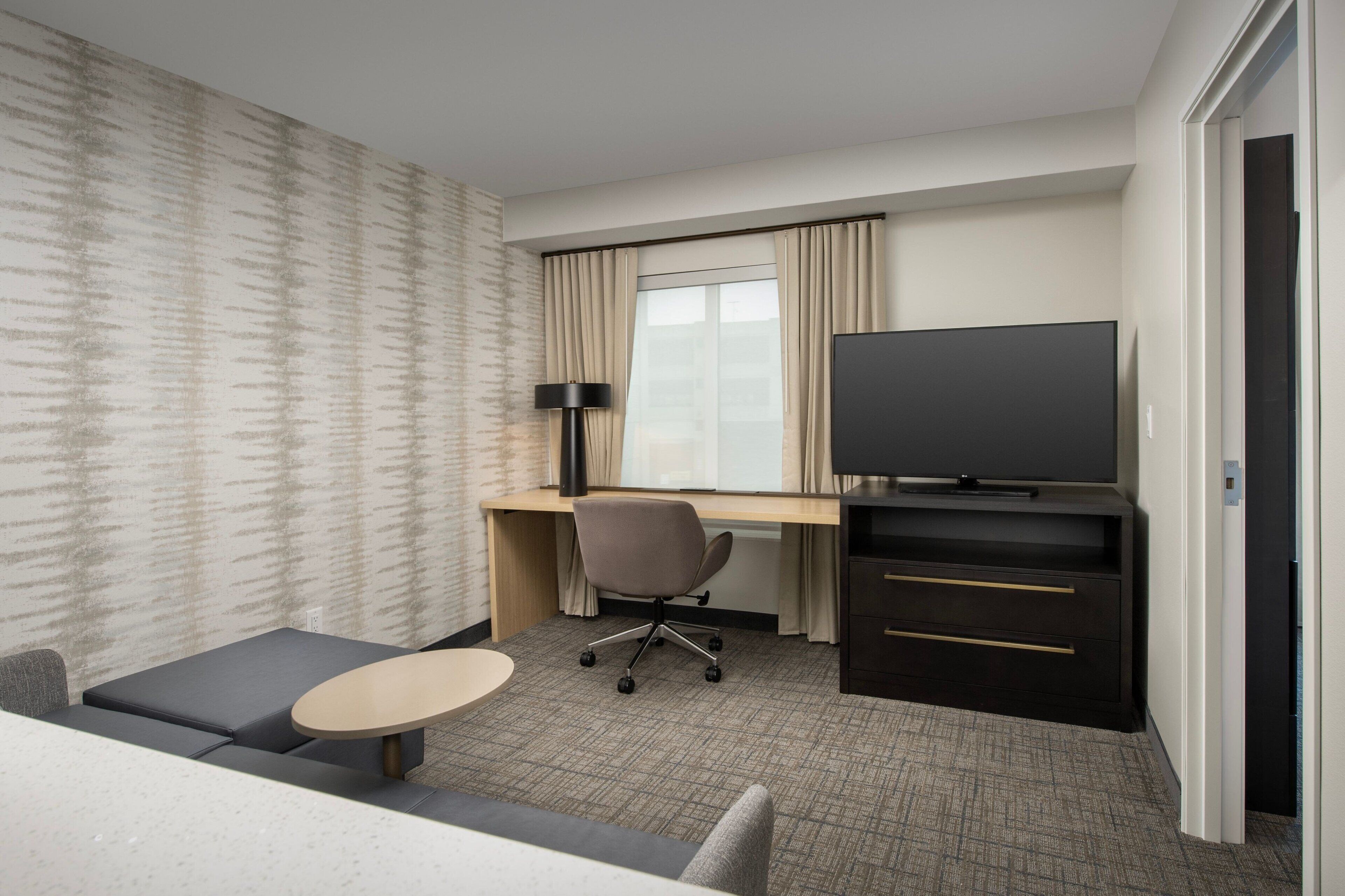 A hotel room with a bed, a desk with a chair, a television, and a small table.
