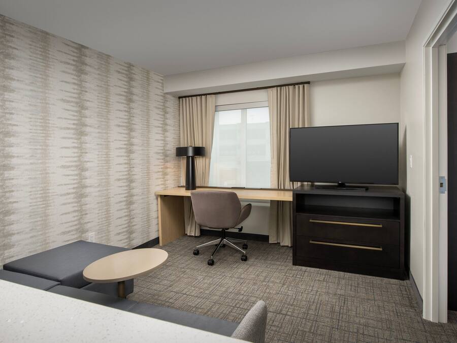 A hotel room with a bed, a desk with a chair, a television, and a small table.