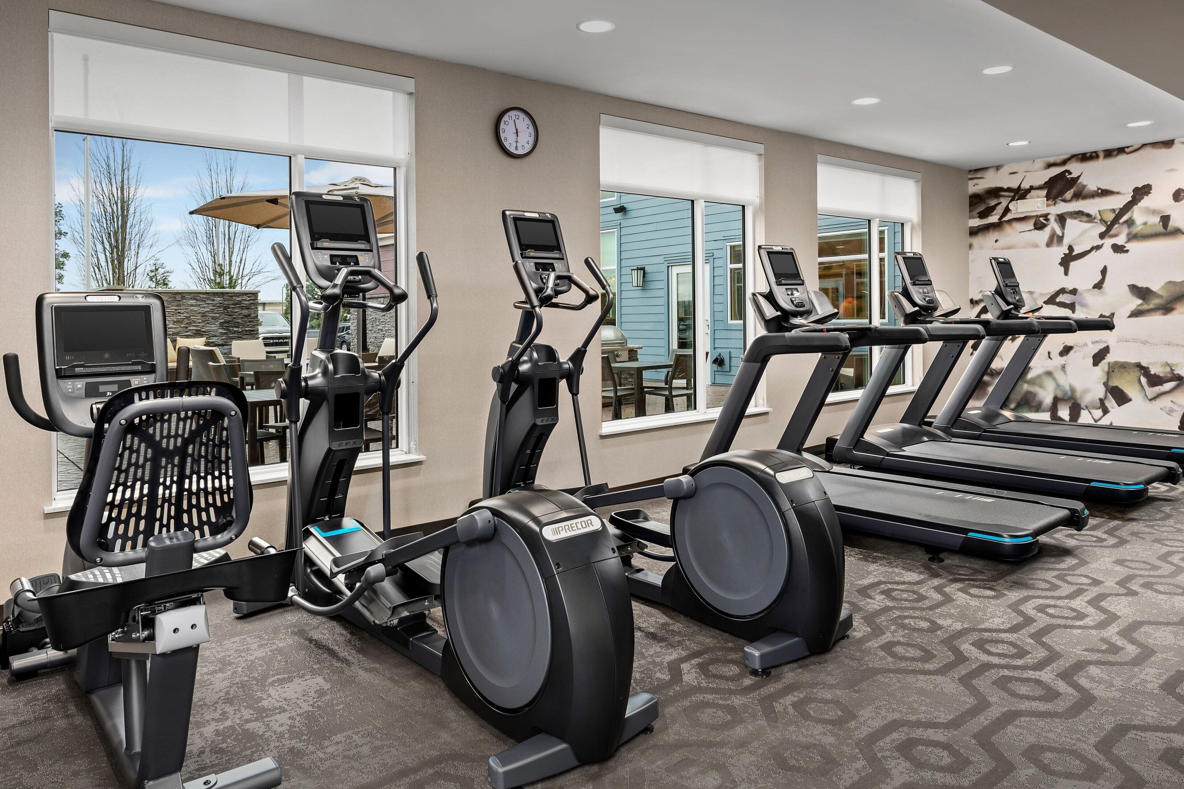 Un gimnasio con cintas de correr, elípticas y una bicicleta estática.