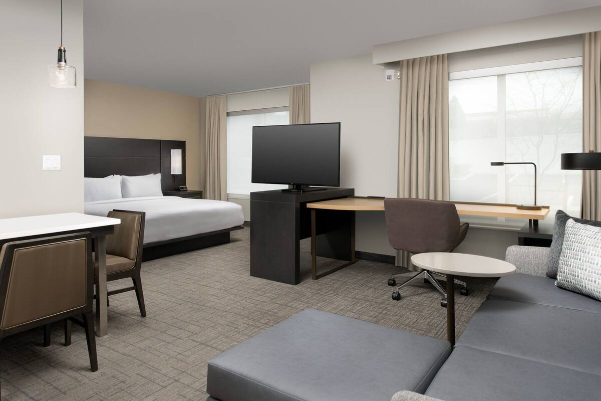 Une chambre d’hôtel comprenant un lit, un bureau avec un téléviseur à écran plat, un canapé, une chaise et une lampe.