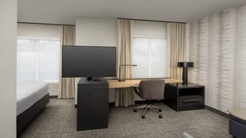 Habitación de hotel con cama, escritorio con computadora, televisor, silla, lámpara y una mesita.