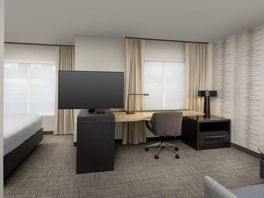 Habitación de hotel con cama, escritorio con computadora, televisor, silla, lámpara y una mesita.