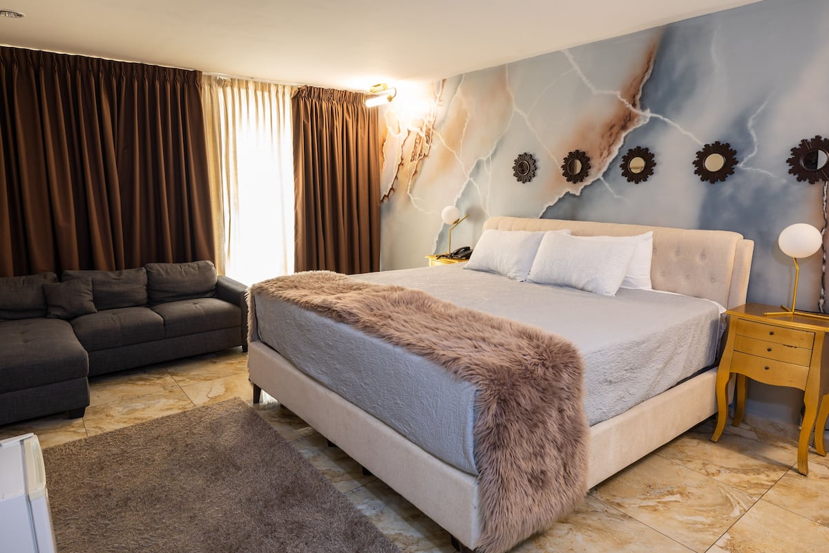 A bedroom with a bed, a sofa, a nightstand, and a wall with a unique design.