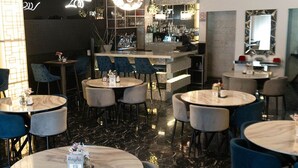 A modern restaurant with round tables and blue chairs, a bar area in the background, and decorative lighting. - Basha Hotel & Restaurant (San Pedro Sula)