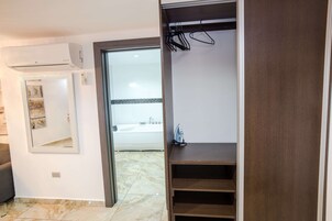 Habitación con aire acondicionado integrado, un espejo, estante de madera y vista al baño con bañera.