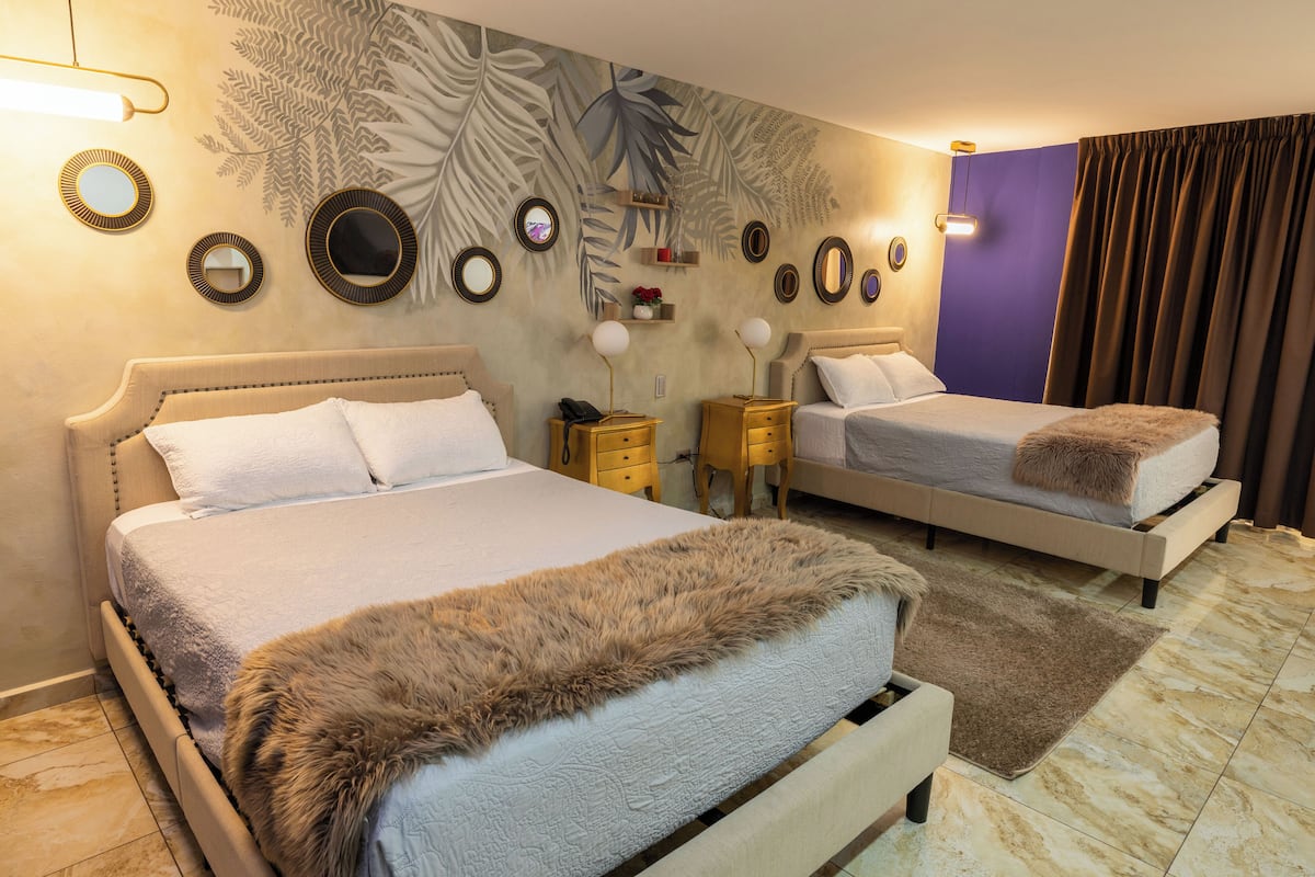 A hotel room with two beds, a large mirror, wall art, and a small table with a lamp.