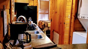 A wooden interior with a kitchen area, including a coffee maker, sink, and a welcome sign. - Hilltop Cabin (Newland)