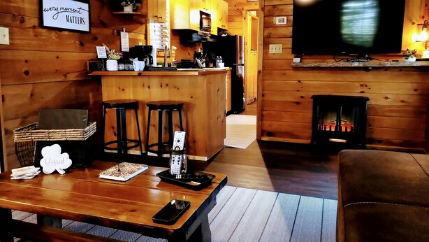 A cozy cabin interior with a wooden interior, a kitchen area, a bar, and a fireplace. - Hilltop Cabin (Newland)