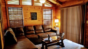 A cozy living room with a brown leather sofa, a wooden coffee table, and a wall-mounted sign. - Hilltop Cabin (Newland)