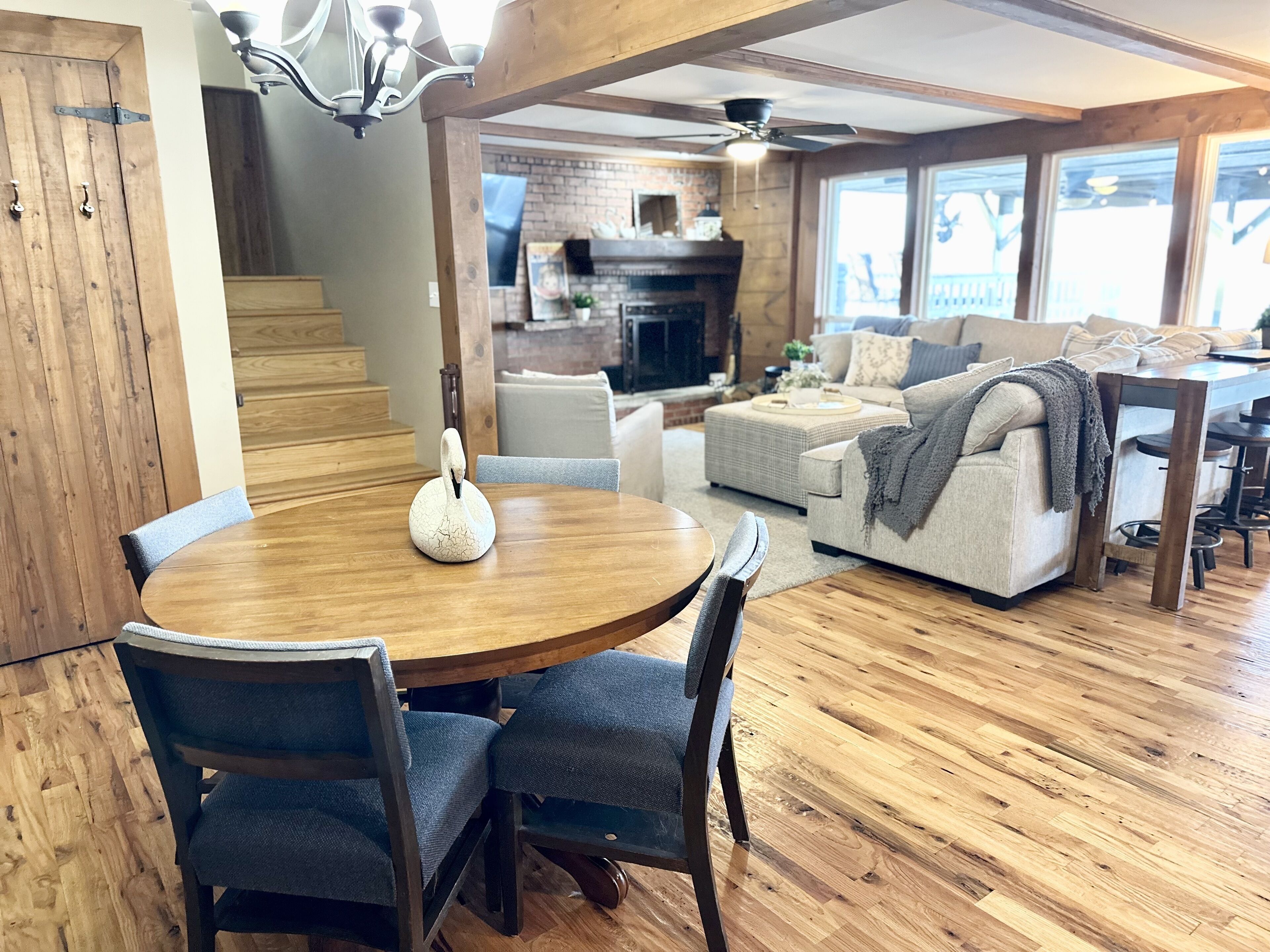 Un comedor con una mesa redonda de madera y sillas, un centro de mesa con forma de cisne y una escalera que conduce a una sala de estar con chimenea y asientos.