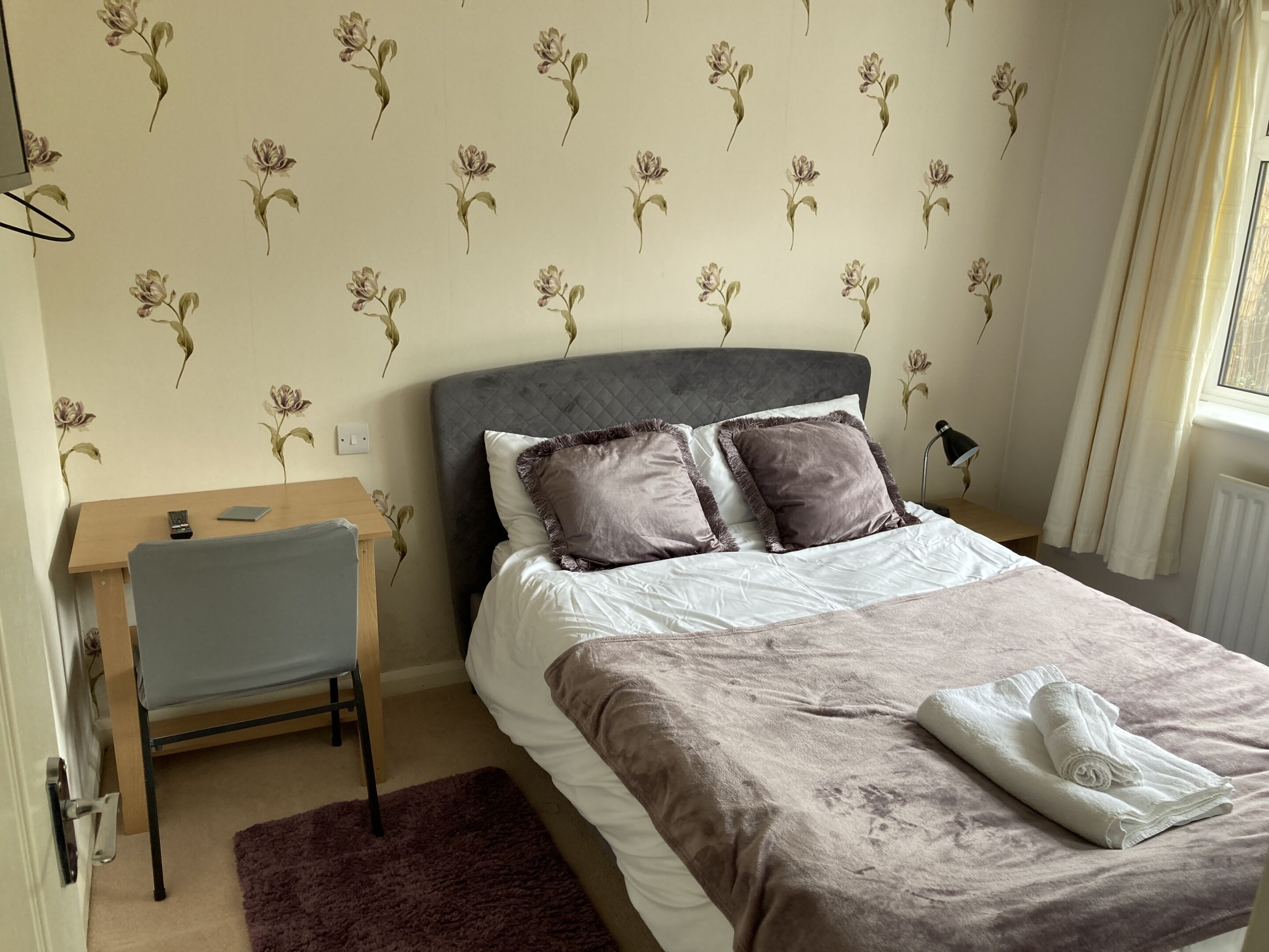 A bedroom with a bed, bedside table, chair, and a window with curtains.