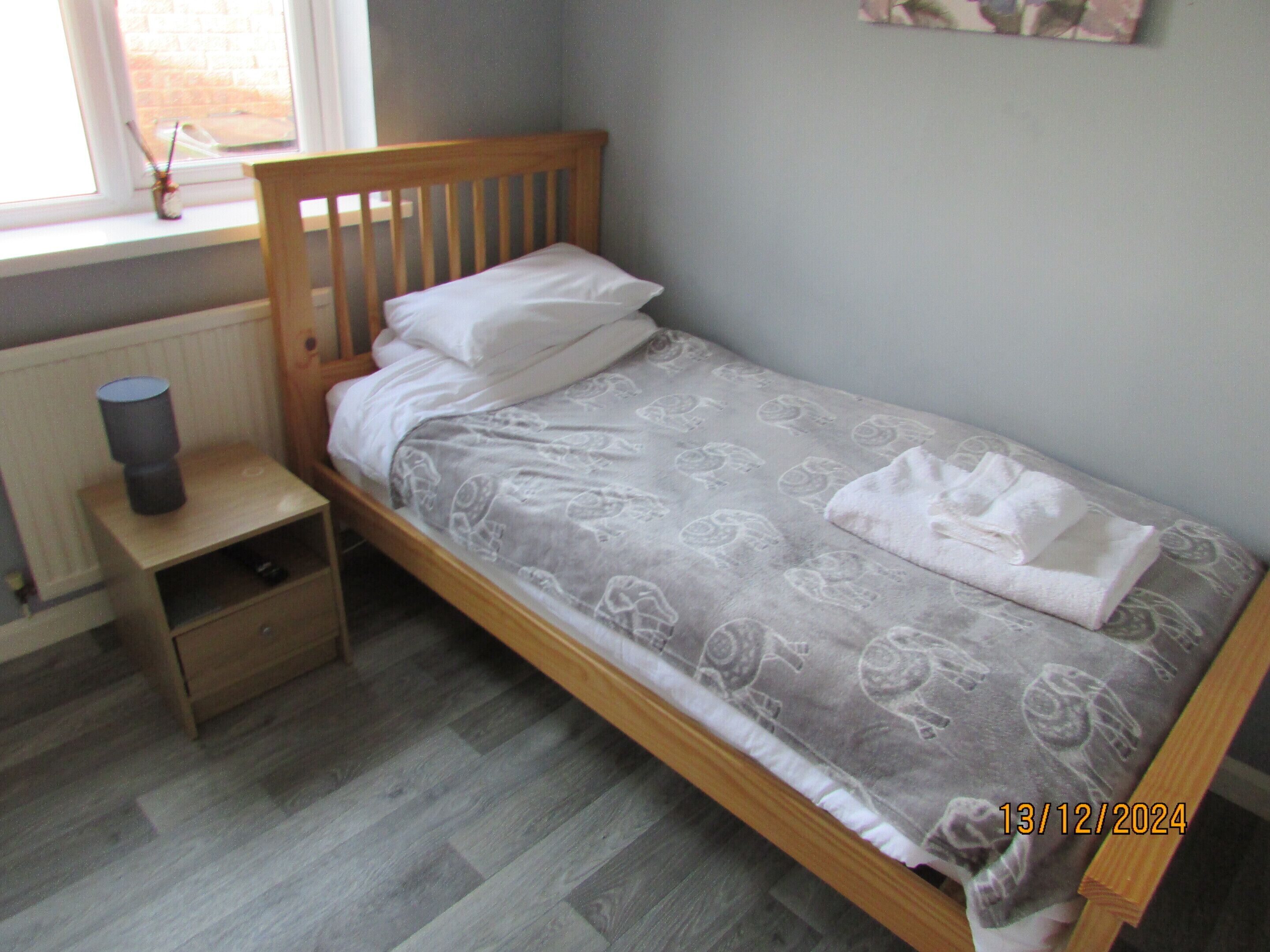 A single bed with a wooden headboard, a bedside table with a lamp, and a radiator under the window.
