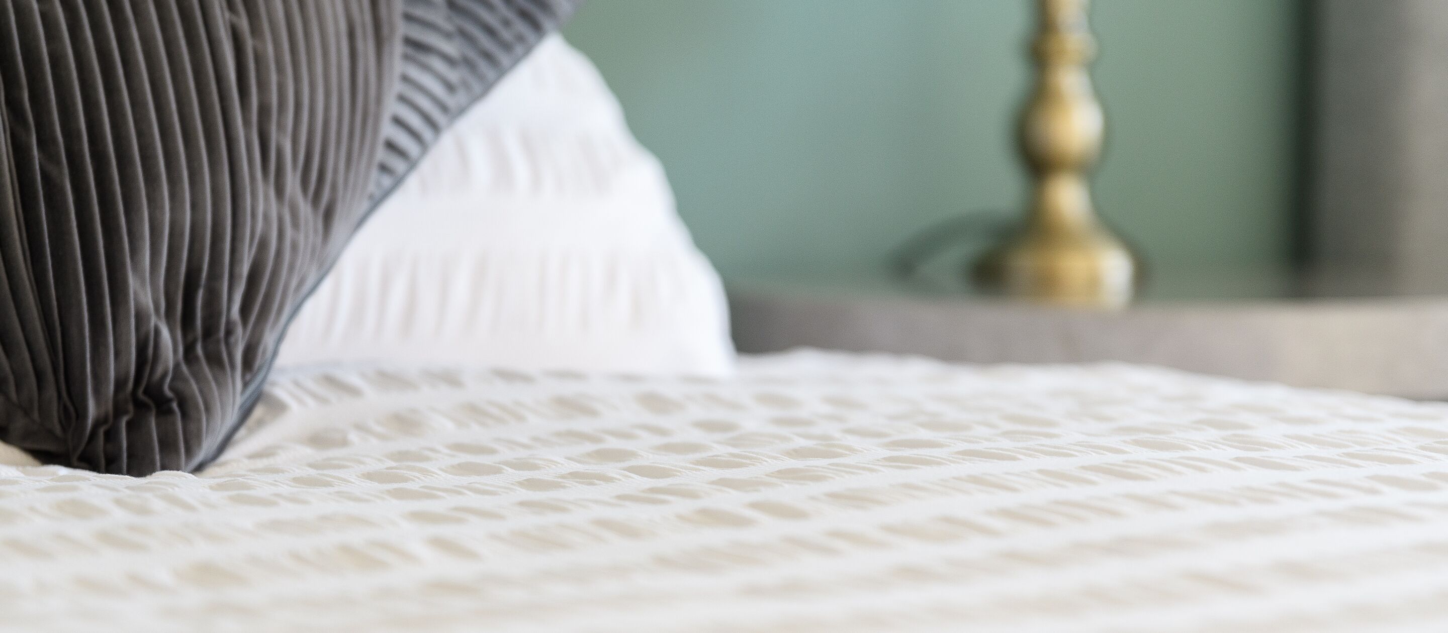 A bed with a textured white bedspread and a dark striped pillow.