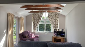A living room with a sofa, a chair, a TV on a wooden stand, and a window with curtains. - Spacious Detached Bungalow With Ample Parking (Grantham)