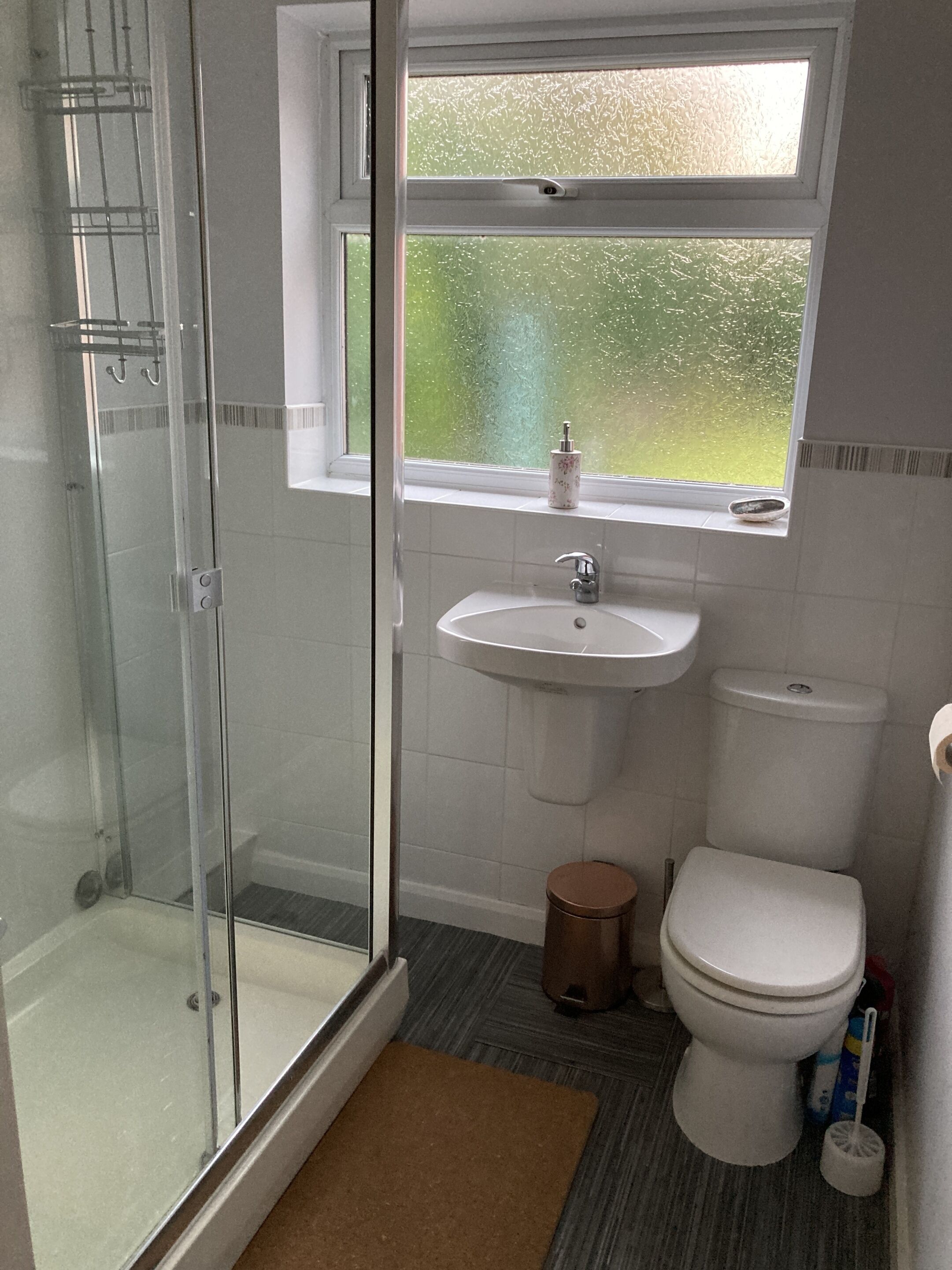 A bathroom with a glass shower enclosure, a sink, toilet, and a window with a view of greenery.