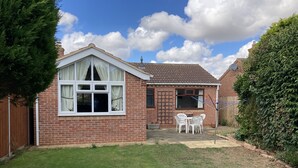 A brick house with a white window, a small patio with a table and chairs, and a garden area. - Spacious Detached Bungalow With Ample Parking (Grantham)