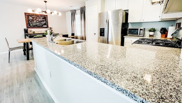 A modern kitchen with a granite countertop, stainless steel appliances, and a dining area with a bench and chairs.