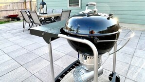 A portable grill with a metal frame and wheels, placed on a tiled patio.