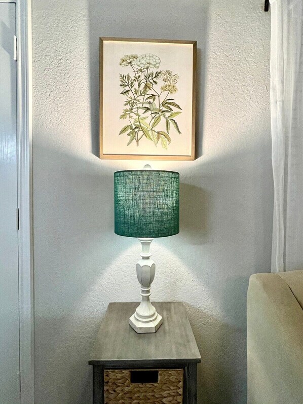 Una lámpara de mesa con pantalla verde con textura sobre una pequeña mesa de madera frente a una pared con textura.