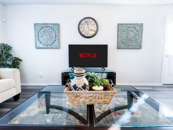 Una sala de estar con una mesa de centro de vidrio, televisor y decoración en la pared.