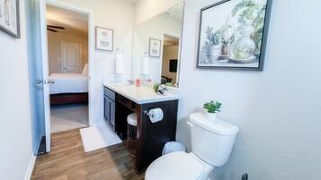 Et lille badeværelse med toilet, vask og en lille bordplade. Et spejl er monteret på væggen, og et billede hænger over vasken.