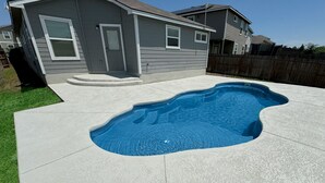 A residential backyard with a swimming pool, a house, and a wooden fence. - Stylish Family Home  Near Lackland  POOL! (San Antonio)
