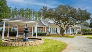 A residential house with a covered porch, a stone fountain, and a well-maintained lawn.