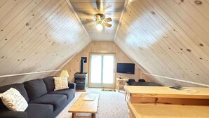 A cozy attic room with a black sofa, a wooden table, a TV, and a ceiling fan.