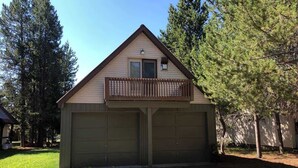 A single-story building with a gabled roof and a balcony. It has two garage doors and is surrounded by trees.