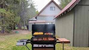 A backyard with a charcoal grill, a wooden table, and a house in the background.