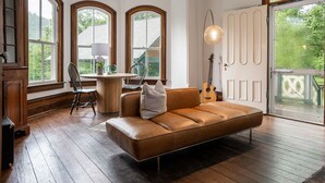 A room with a brown leather sofa, a wooden dining table with chairs, and large arched windows. - Magnolia House estate - family reunions, micro-weddings, retreats. (Hot Springs)