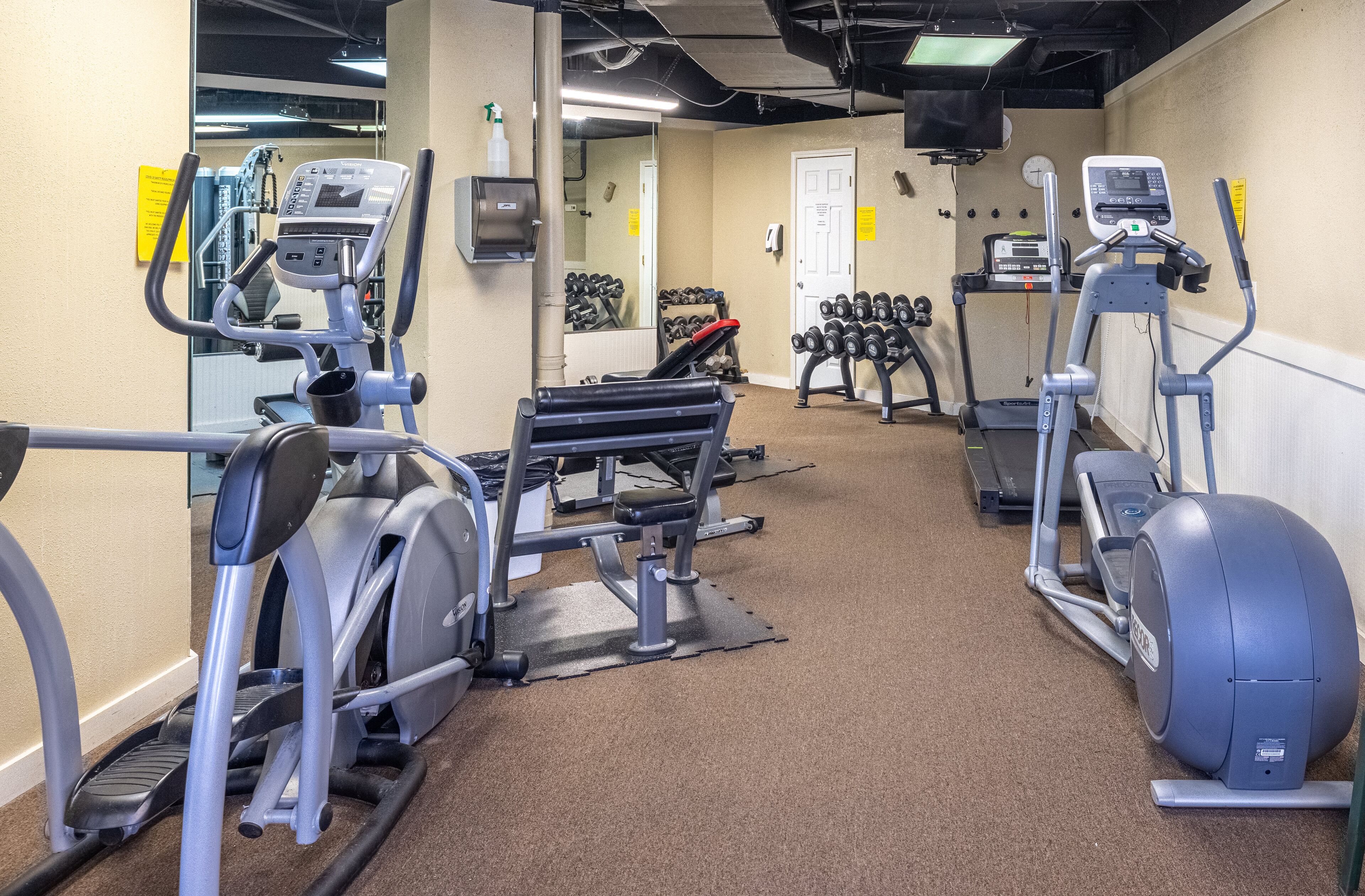 A gym with various cardio and strength training equipment, including treadmills, elliptical machines, and dumbbells.