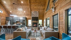 Interior acogedor de una cabaña con chimenea de piedra, paredes de madera y una zona de comedor con taburetes de bar.