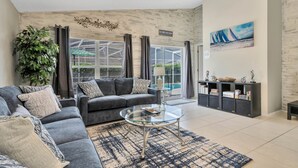 A modern living room with a gray sofa, a glass coffee table, and a bookshelf. - Spacious House, Near Disney, 4BDR & 3bath Sleeps up to 10,Game Room+ Heated Pool (Davenport)