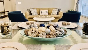 A modern living room with a beige sofa, two blue armchairs, a glass coffee table, and decorative items including a bowl of woven balls and a glass jar of pebbles. - Spacious House, Near Disney, 4BDR & 3bath Sleeps up to 10,Game Room+ Heated Pool (Davenport)