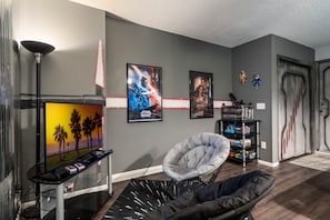 A living room with a flat-screen TV, a bean bag chair, a gaming chair, and a shelf with toys. - Spacious House, Near Disney, 4BDR & 3bath Sleeps up to 10,Game Room+ Heated Pool (Davenport)