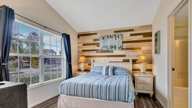 A bedroom with a large bed, two bedside tables, a window with curtains, a wooden wall panel, and a door. - Spacious House, Near Disney, 4BDR & 3bath Sleeps up to 10,Game Room+ Heated Pool (Davenport)