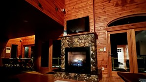 Un intérieur chaleureux avec une cheminée en pierre, des murs en bois et un téléviseur à écran plat fixé au-dessus.