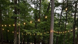 Un bain à remous entouré de sièges d’extérieur et illuminé de guirlandes lumineuses, le tout situé dans un espace boisé.