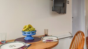 Une table à manger avec un saladier de fruits, des assiettes et des couverts. Une chaise est placée près de la table.