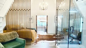 Une chambre spacieuse située dans les combles, avec un plafond haut, une grande fenêtre, un canapé vert, un tapis en cuir marron et une cloison en verre.