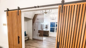 Un intérieur moderne avec un plancher en bois, une porte coulissante, un escalier et un coin cuisine visible à travers une cloison.