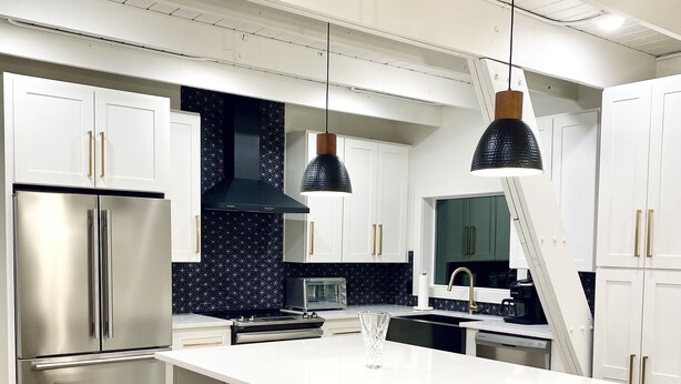 Une cuisine moderne avec des meubles blancs, un réfrigérateur en acier inoxydable, un pare-feu noir et blanc et un îlot central doté de tabourets de bar.